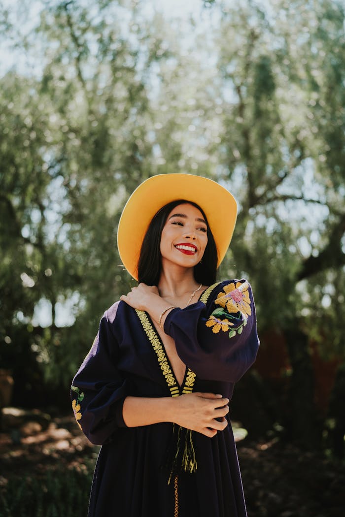 The Art of Drawing Readers In: Your attractive post title goes here Smiling woman wearing a traditional embroidered dress and yellow hat, enjoying a sunny day outdoors.
